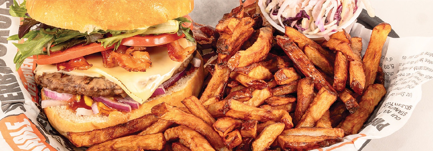 Le burger du Stanley, fromage fondu, tomate et oignon rouge, avec frites maison dans un papier imprimé « Sherbrookois »