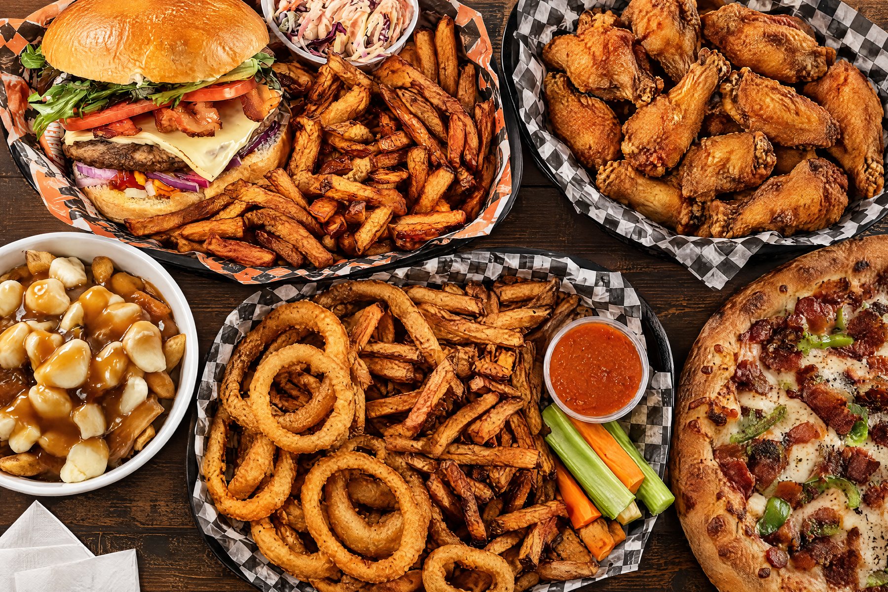 Une table de bois couverte de plats du Stanley : le panier burger et frites, les ailes, la poutine, le Tour du chapeau et une pizza