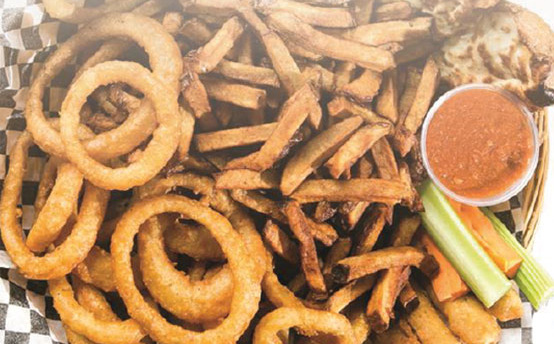 Rondelles d'oignon, frites et bâtonnets de céleri dans un panier à carreaux, avec une sauce
